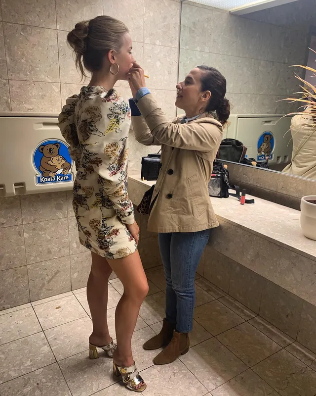 Willa Fitzgerald having makeup applied while wearing metallic heels.