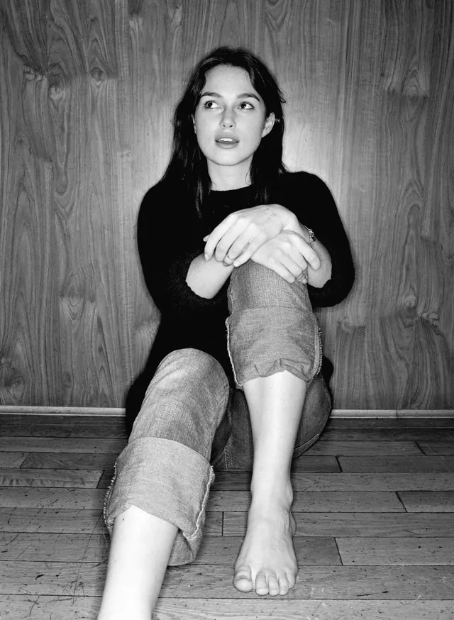 Keira Knightley a monochrome seated portrait against a wooden wall.