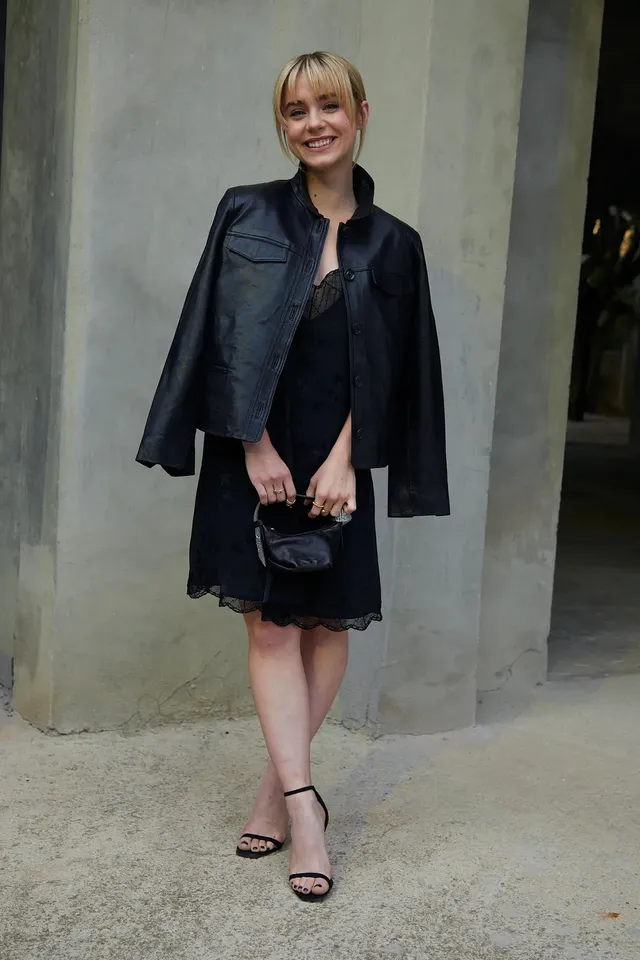 Clara Galle posing in a black dress, leather jacket and strappy heels.