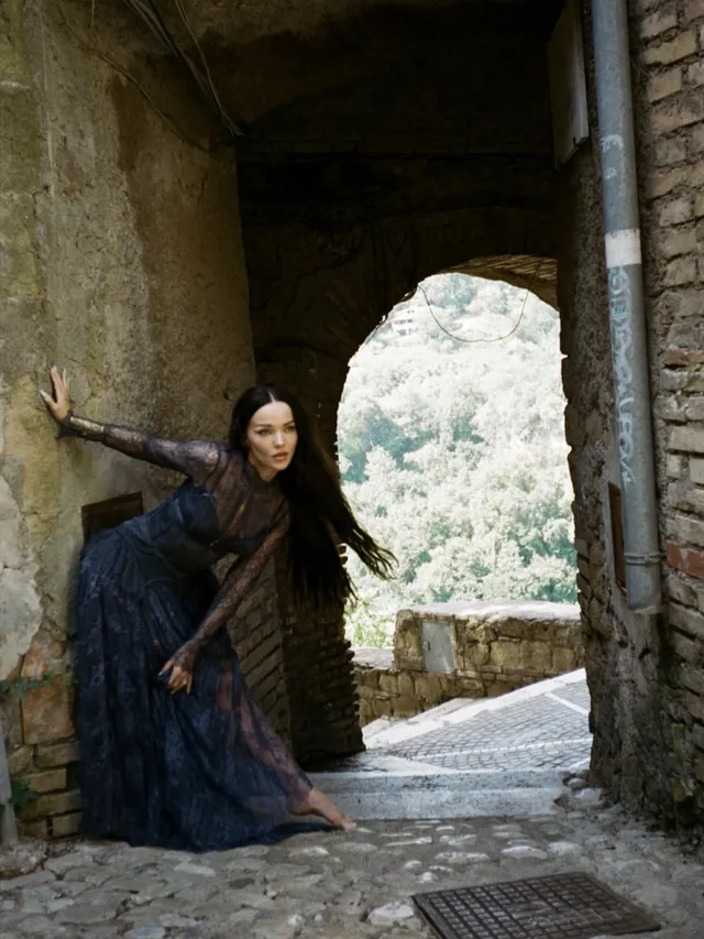 Dove Cameron posing barefoot beside a stone archway.
