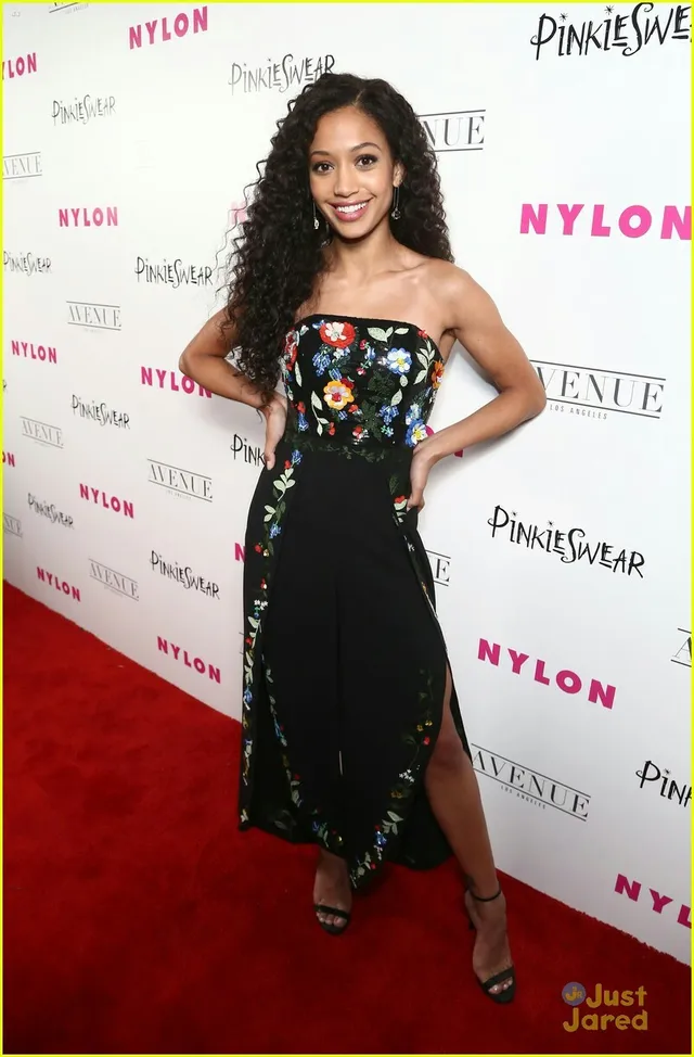 Samantha Logan posing in a black floral dress and heels on a carpet.