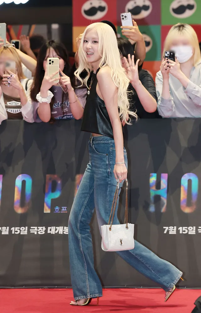Rosé waving at a premiere in a black sleeveless top and jeans with a small white handbag.
