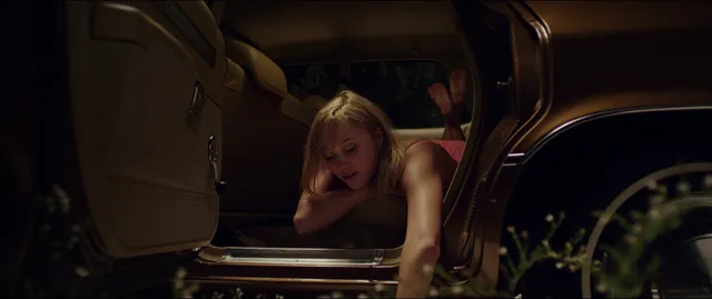 Maika Monroe reaching barefoot out of a vehicle in a scene.