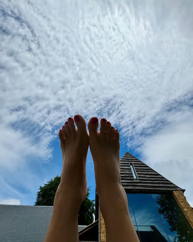Salma Hayek raising her bare feet toward a cloudy sky.