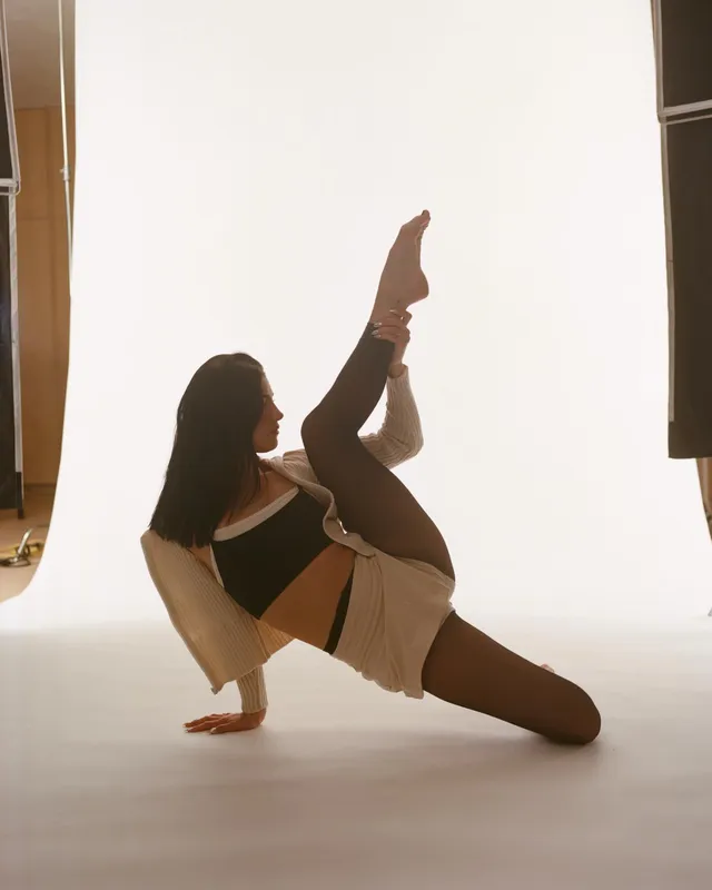 Charli D’Amelio holding a barefoot studio pose with one leg raised.