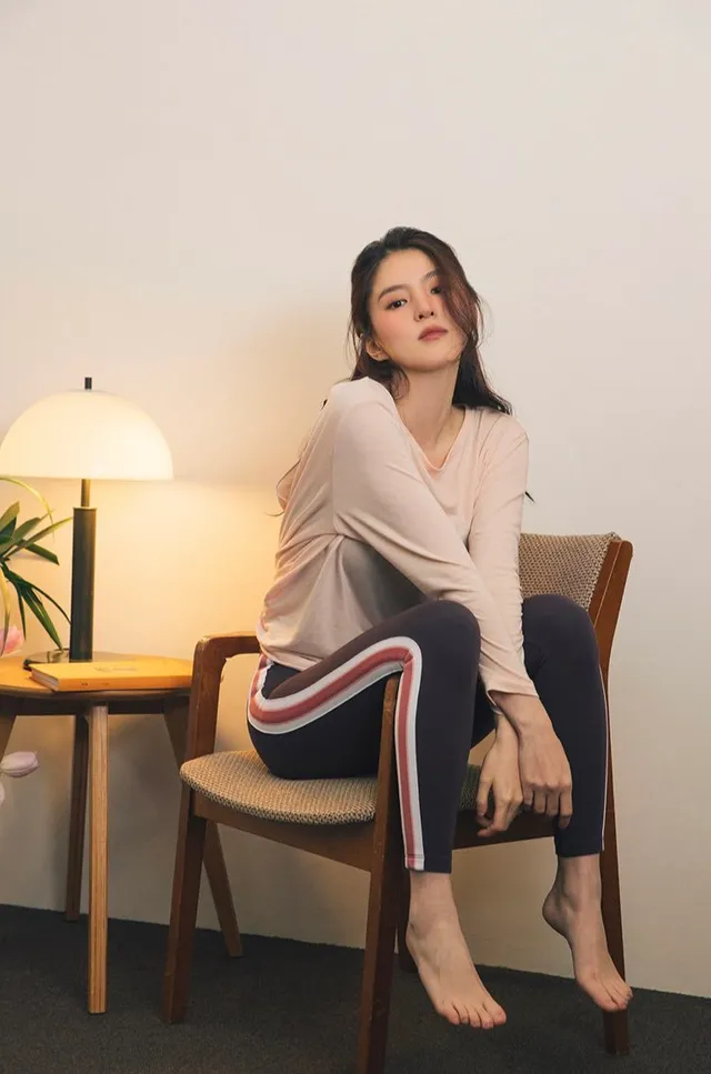 Han So-hee sitting barefoot in a white top and striped trousers.