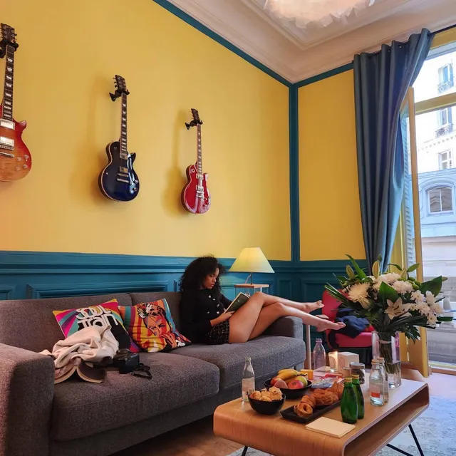 Whitney Peak reclining barefoot on a sofa in a colorful room.