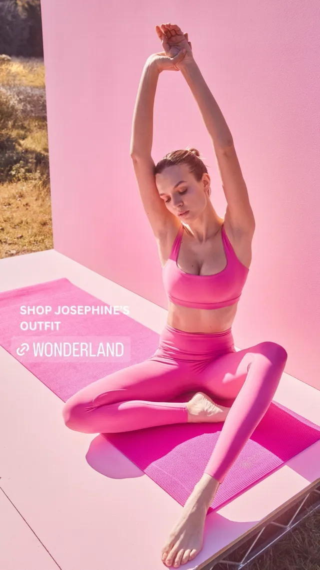 Josephine Skriver sitting barefoot in a hanging chair wearing a pink exercise outfit.