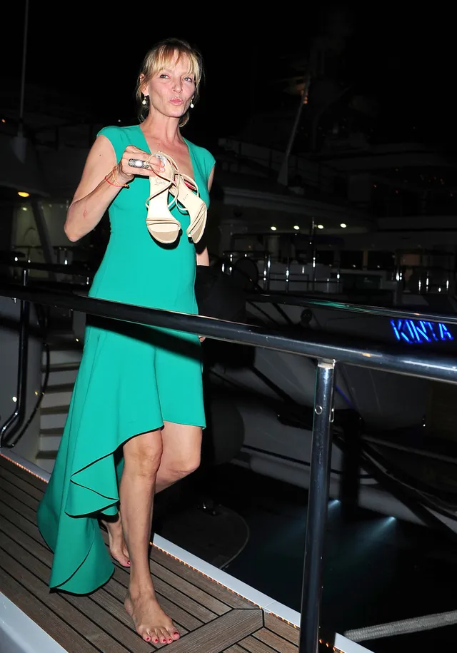 Uma Thurman standing barefoot in a green dress.