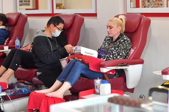 Gwen Stefani sitting at a nail salon with bare feet resting on a towel.