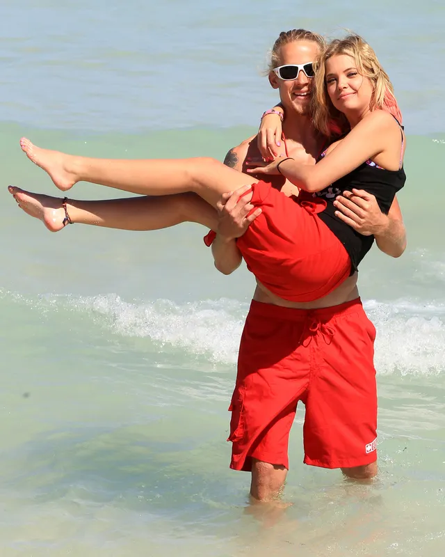Ashley Benson being carried by a companion at the shoreline.