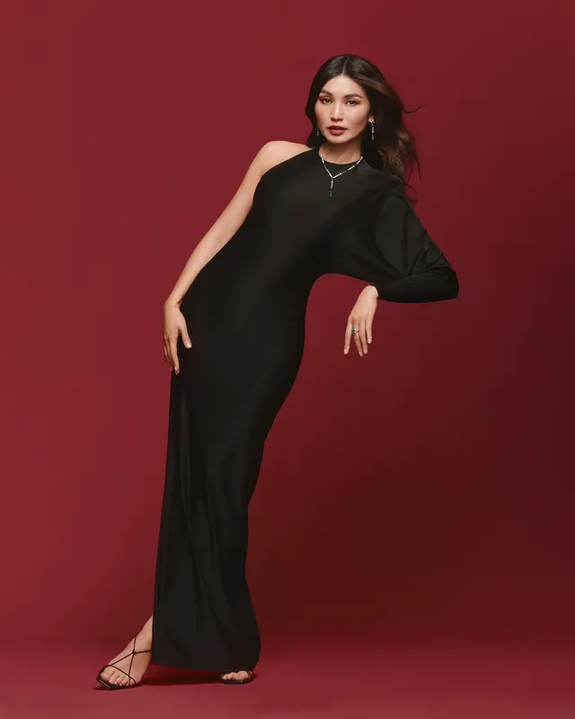 Gemma Chan posing in a black gown against a red backdrop.