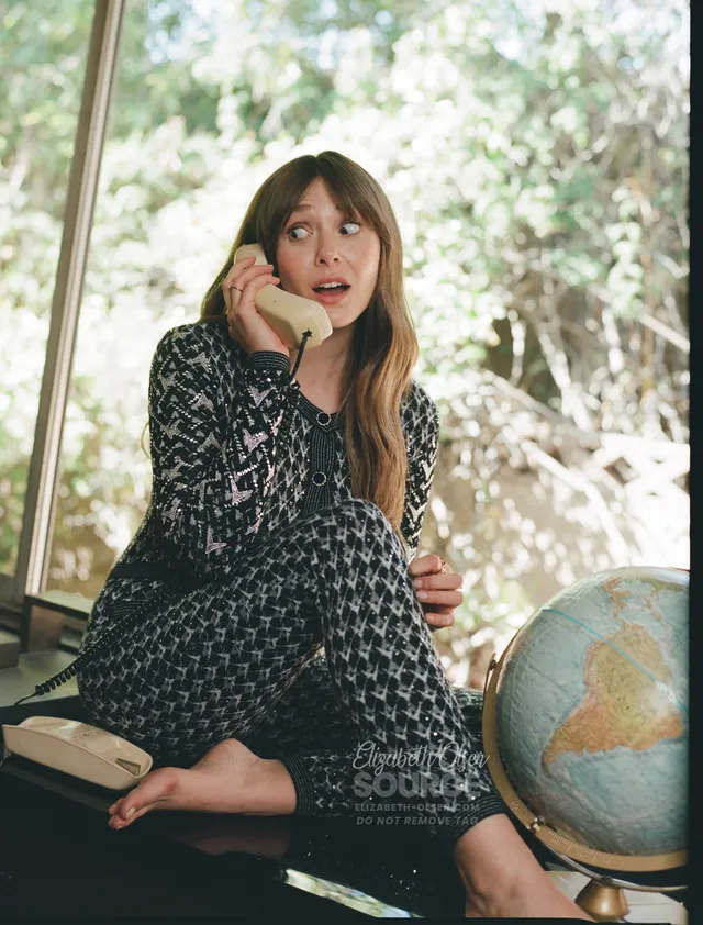 Elizabeth Olsen sitting barefoot beside a globe and holding a phone.