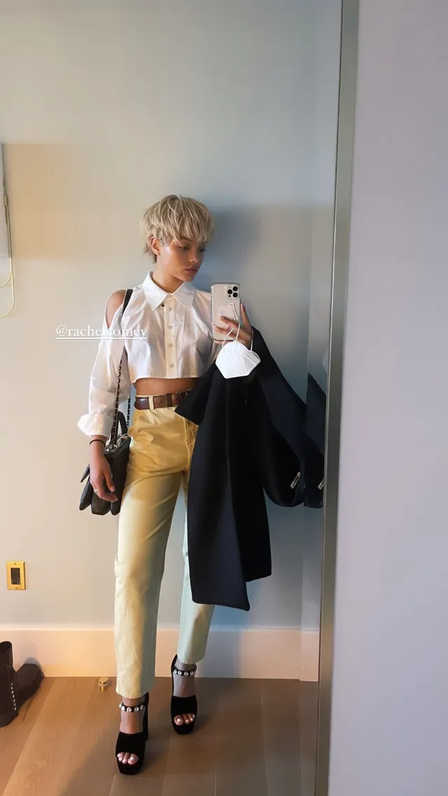 Whitney Peak taking a mirror selfie in a white shirt, pale trousers and black heels.