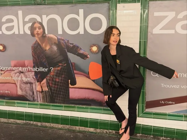 Lily Collins balancing beside an advertising wall in a black suit and heels.