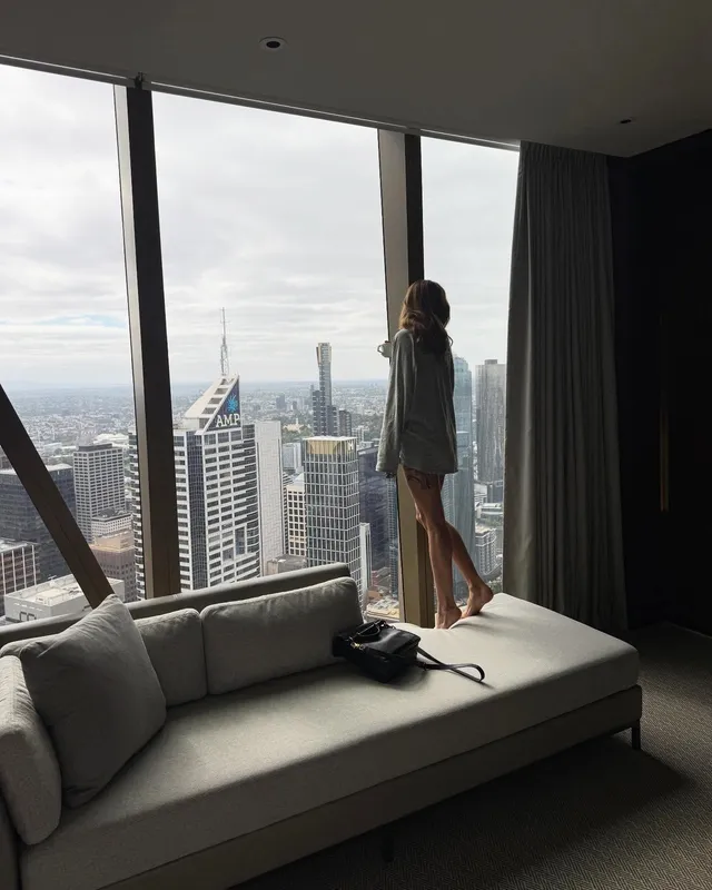 Debby Ryan standing beside a window overlooking a city.