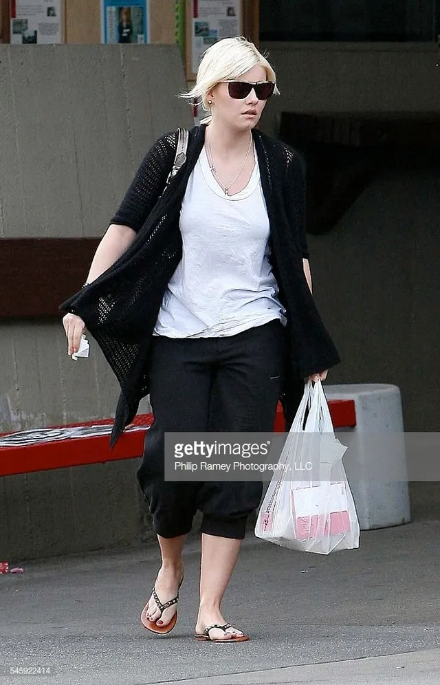 Elisha Cuthbert walking outdoors in a black cardigan, cropped trousers and flip-flops.
