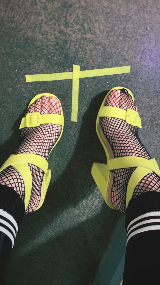 Meg Donnelly shown from above wearing yellow sandals and fishnet socks.