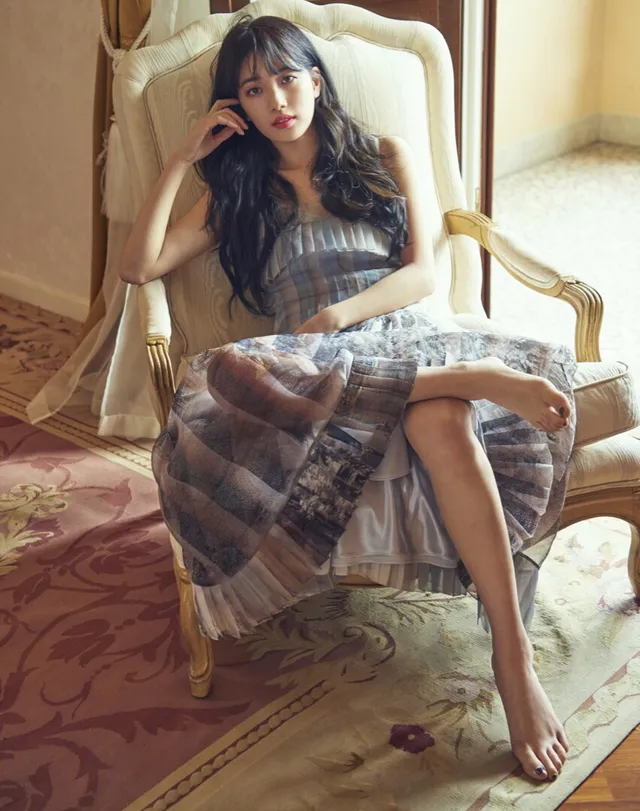 Bae Suzy sitting in a printed dress and pale heels.