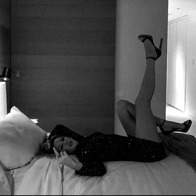 Ellie Goulding reclining on a bed with a black heel raised in a monochrome photograph.