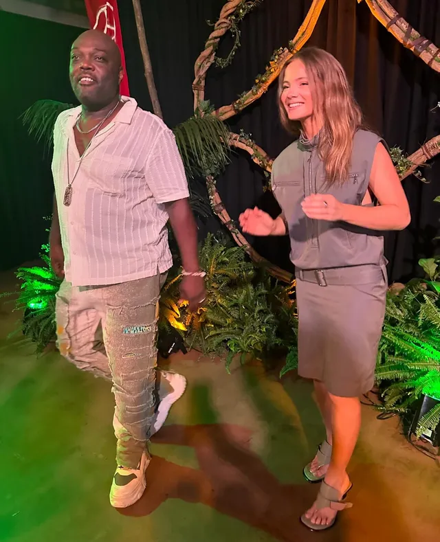Freya Allan posing beside a man in a grey outfit and metallic heels.