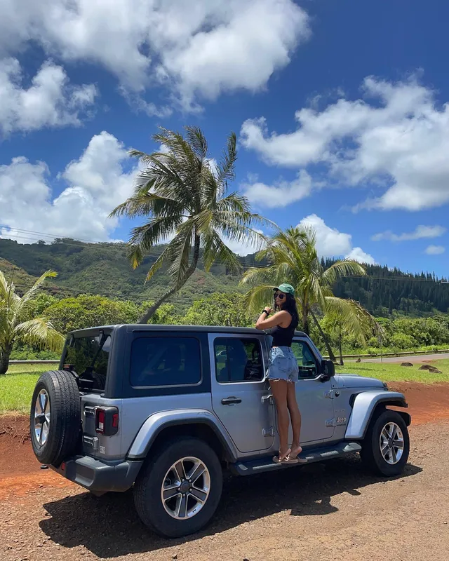Greta Onieogou standing on a vehicle outdoors in denim shorts and flat sandals.