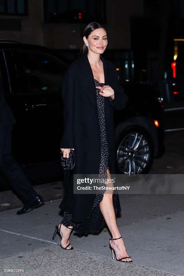 Phoebe Tonkin walking outside in a dark dress and heels.