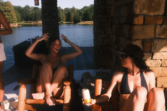 Madelyn Cline sitting with friends beside a lake in swimwear.