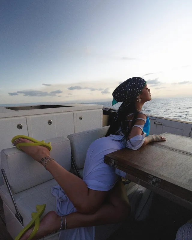 Rihanna leaning across a boat bench while wearing bright yellow sandals.