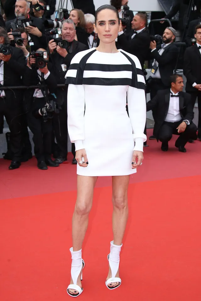 Jennifer Connelly posing at a film festival in a white dress and ankle boots.