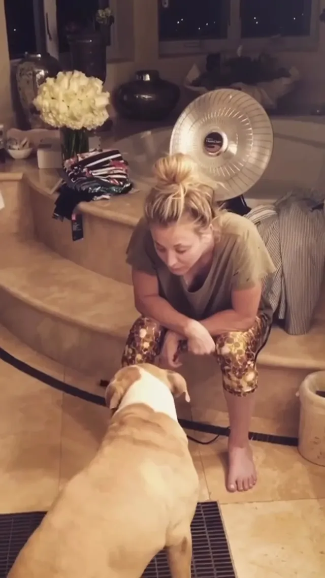Kaley Cuoco kneeling barefoot beside a dog.