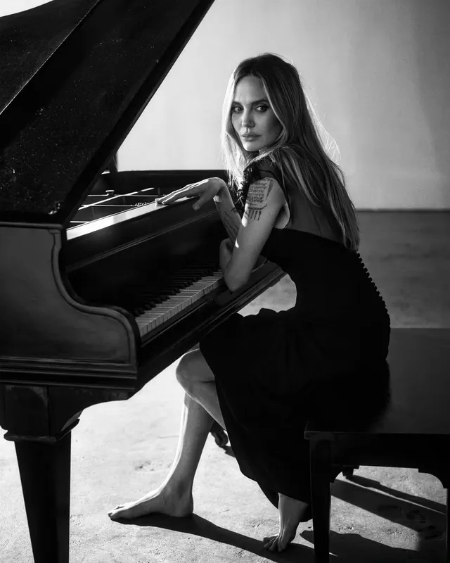 Angelina Jolie a monochrome portrait seated beside a piano.