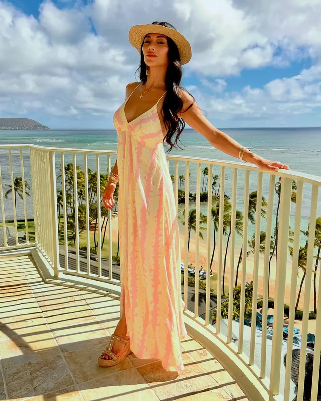 Nicole Scherzinger standing on a balcony in a long floral dress and platform heels.