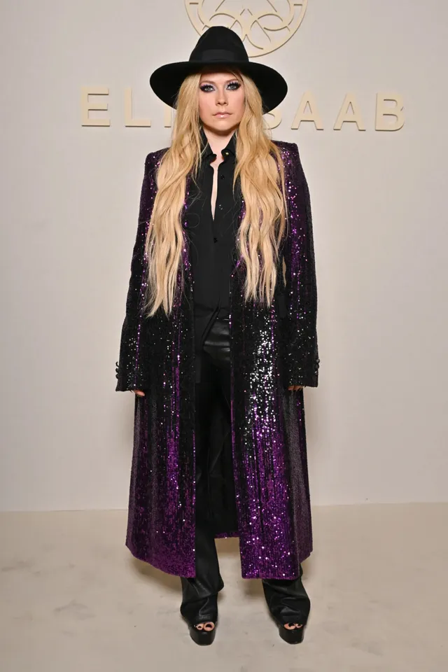Avril Lavigne posing at an event in a long coat and platform heels.