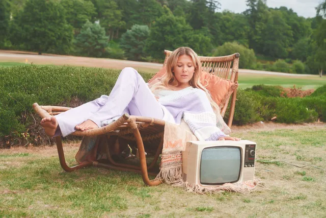 Millie Bobby Brown: reclining barefoot on a garden chair beside a small television.