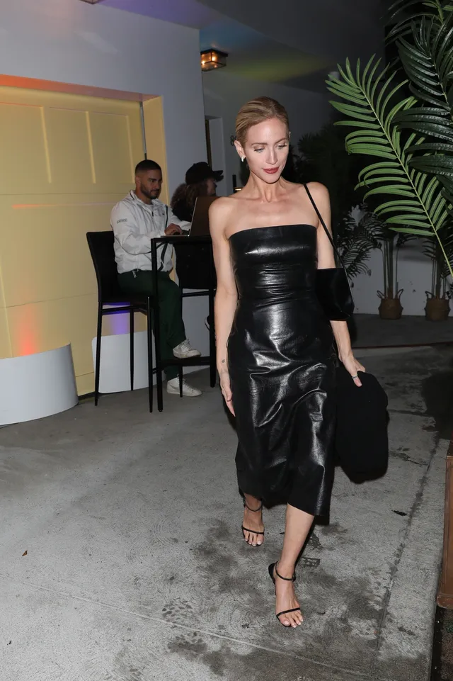 Brittany Snow walking outside in a black satin dress and sandals.