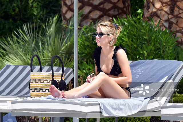 Emma Roberts sitting barefoot on a sun lounger in black swimwear.