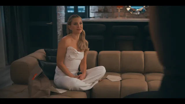 Kate Hudson sitting cross legged on a sofa in a screen scene.