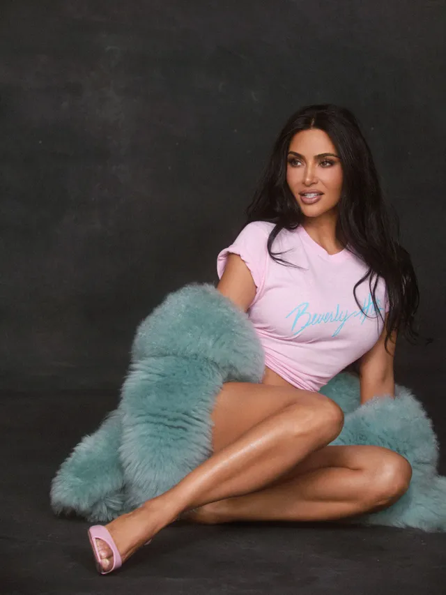 Kim Kardashian sitting on a floor wearing a pink outfit and pink heels.