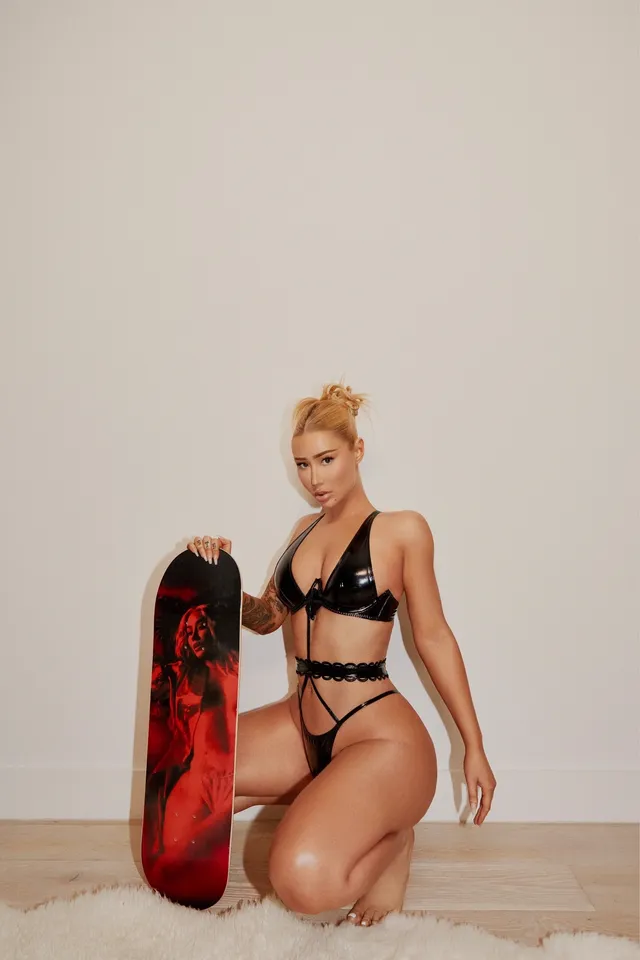 Iggy Azalea kneeling barefoot beside a skateboard.