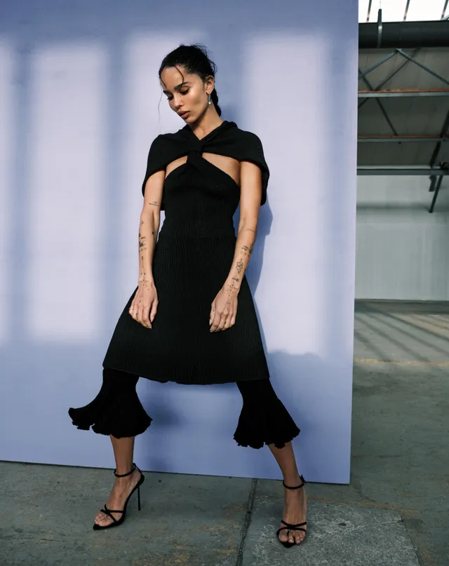 Zoë Kravitz posing in a black dress against a purple backdrop.