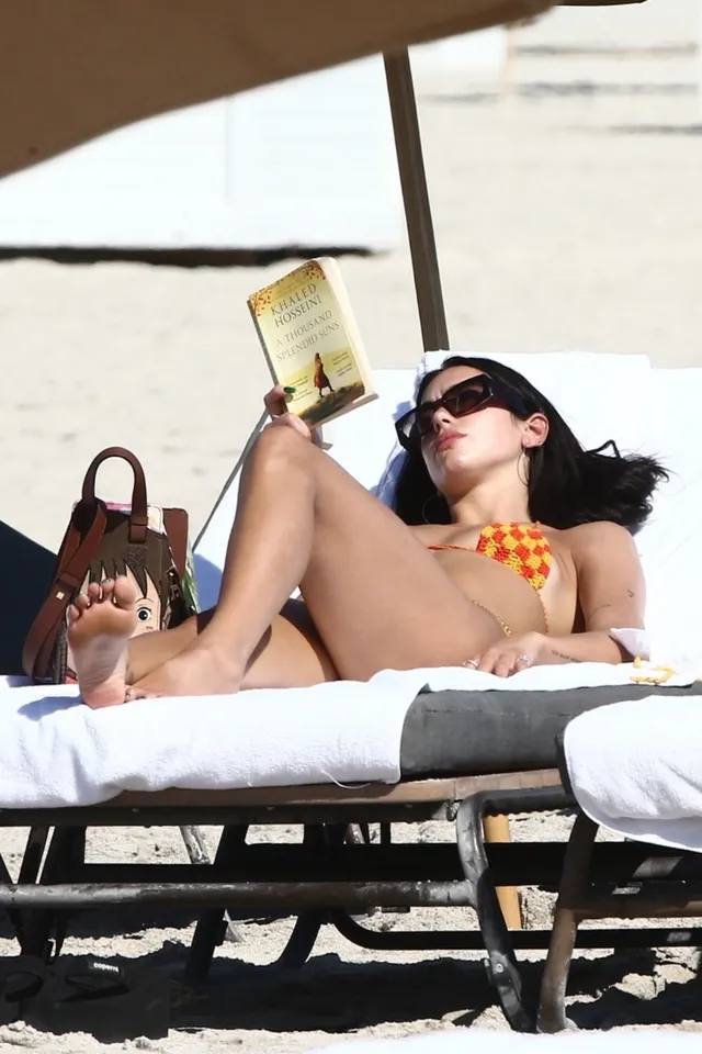 Dua Lipa resting barefoot on a white sun lounger.
