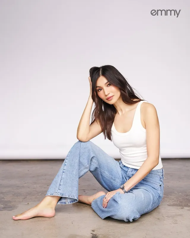 Gemma Chan sitting on the floor in jeans and a white top.
