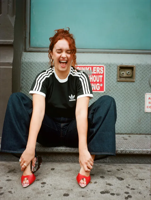 Olivia Cooke crouching in jeans and red mules.