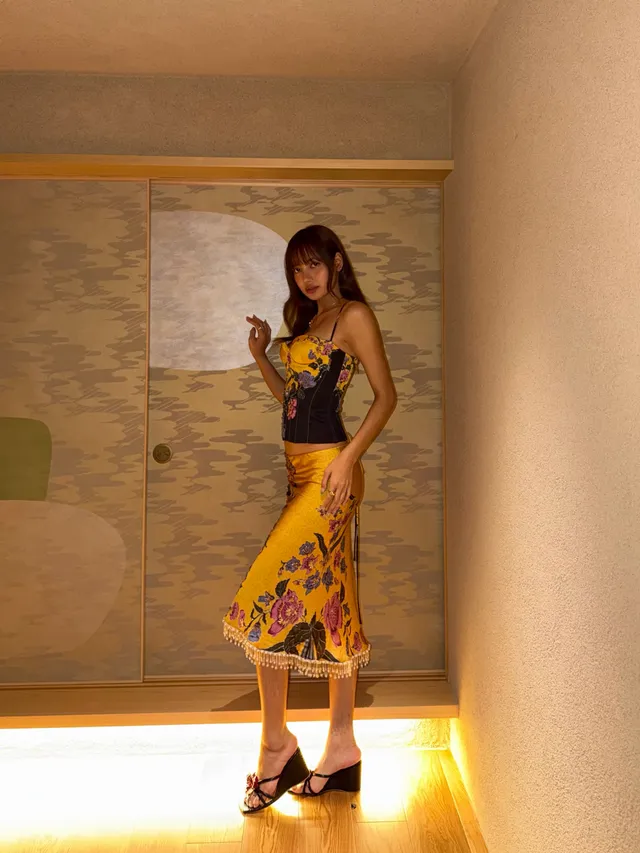 Lisa (Lalisa Manobal) standing in black heels and a patterned skirt beside a tiled wall.