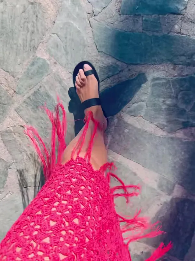 Gal Gadot wearing black flip-flops beneath a pink dress.