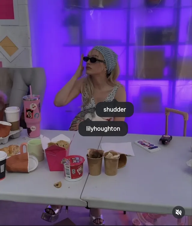 Victoria Pedretti sitting behind a table wearing casual sandals.