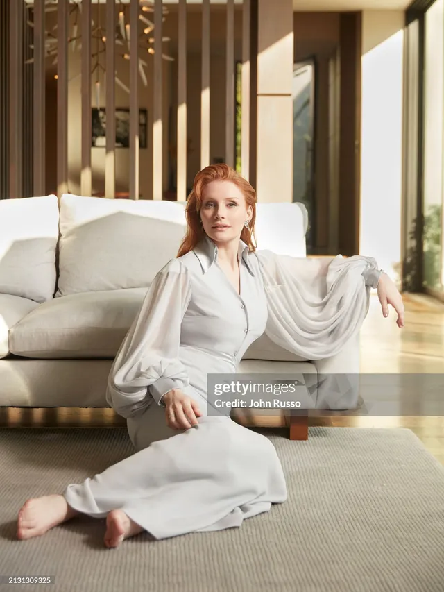 Bryce Dallas Howard sitting on a sofa in a pale flowing outfit.