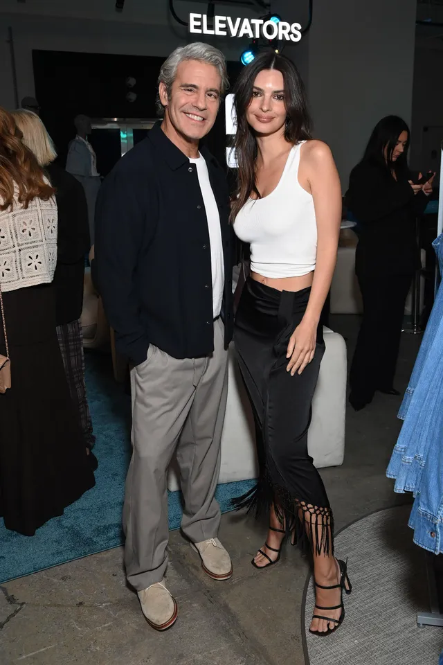 Emily Ratajkowski posing beside a man wearing a white top and black heels.