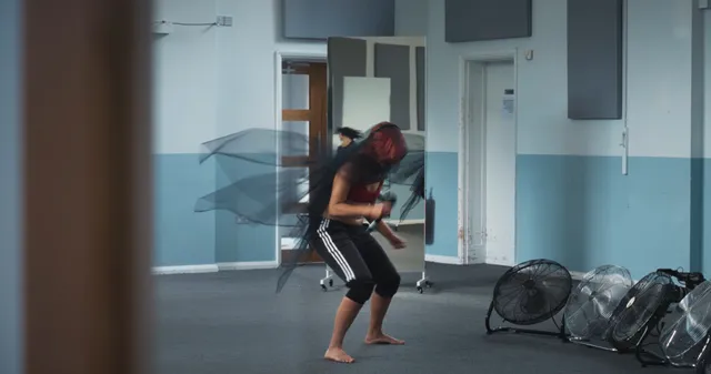 Naomi Scott kneeling barefoot in a rehearsal room.